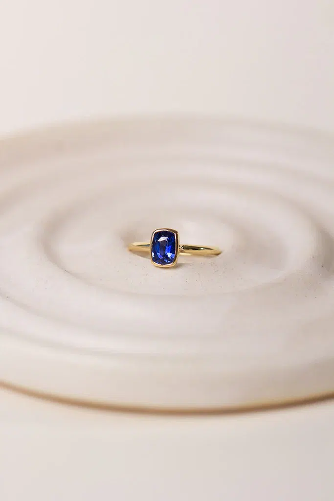 Anillo de zafiro cushion en oro sobre superficie cerámica — Sakti Atelier